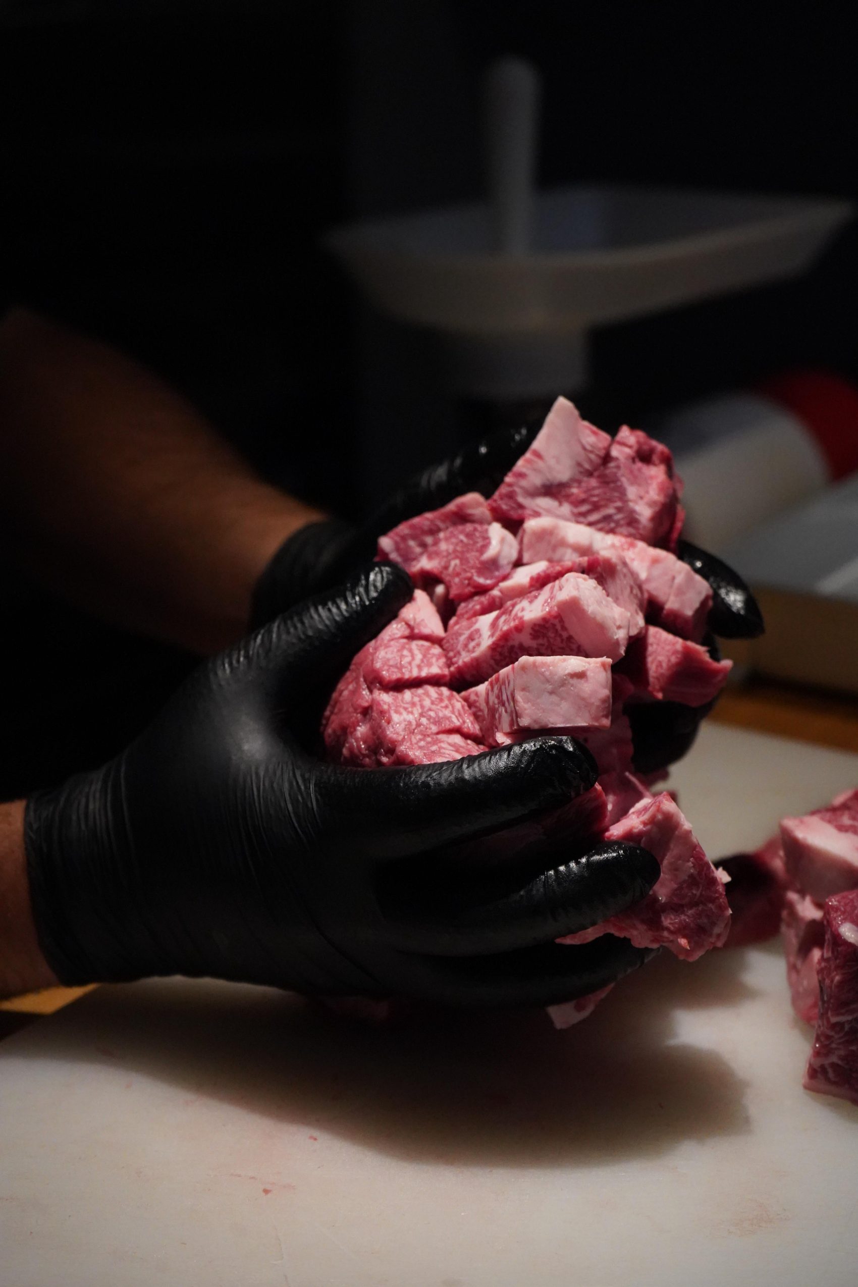 Gloved hands cradling cubes of raw wagyu