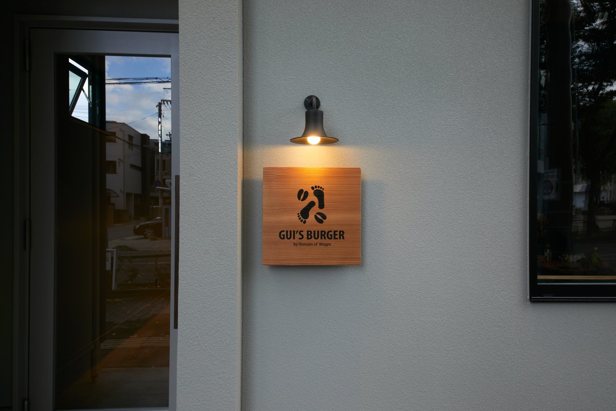 The Gui&rsquo;s Burger wooden signboard glowing under a lamp at dusk